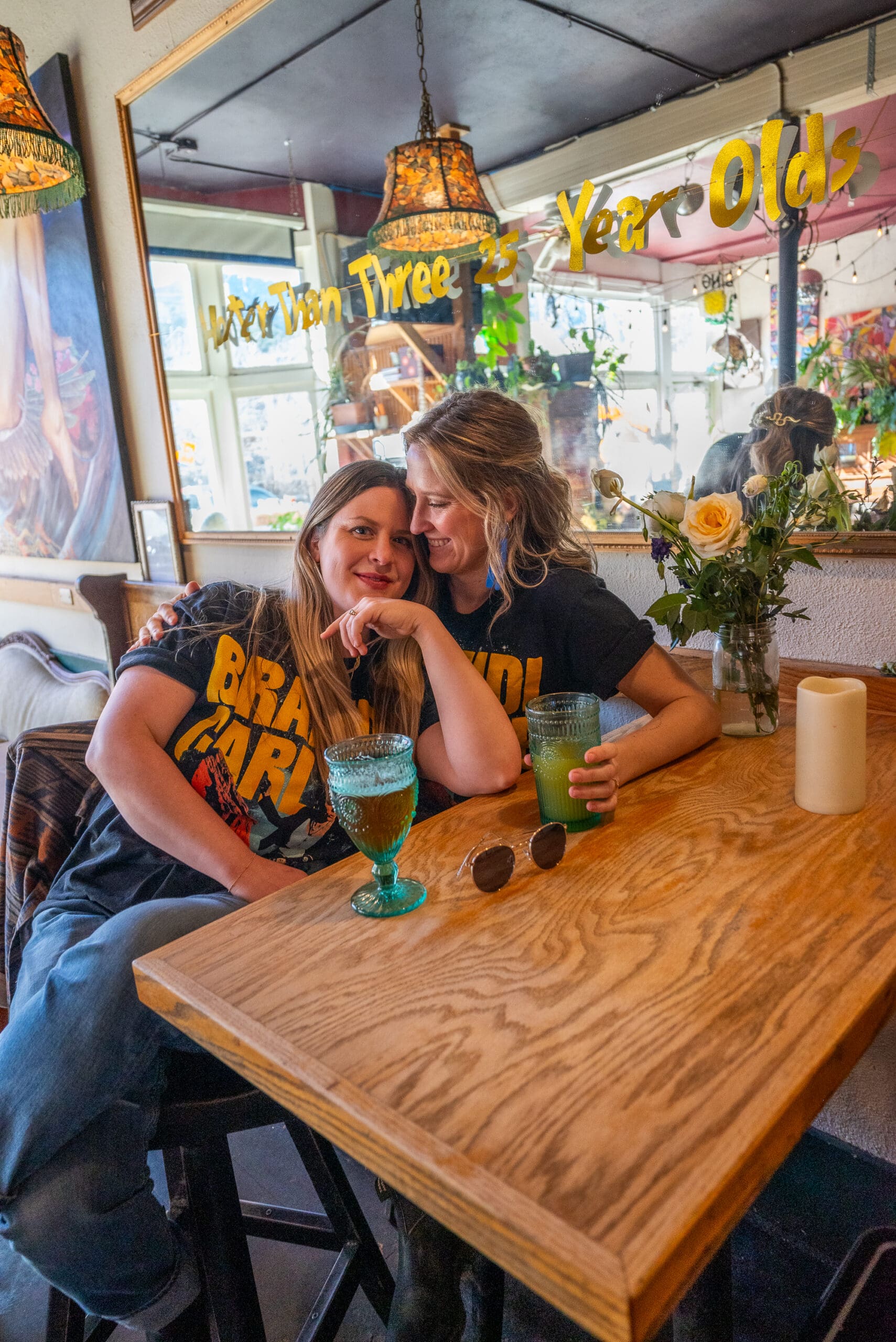 female couple sit in a local dive bar with beers, they cuddle and soak in the moment.